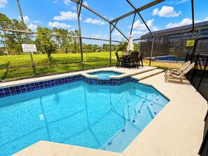 A swimming pool with a glass enclosure, surrounded by a grassy area and trees. - Beautiful Pool Home With Spa Overlooking Golf Course (Davenport)