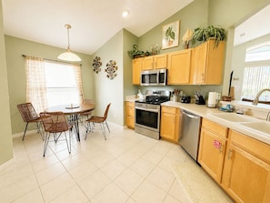 A kitchen with wooden cabinets, a microwave, stove, oven, and a sink. There is a dining table with chairs and a window with curtains. - Beautiful Pool Home With Spa Overlooking Golf Course (Davenport)