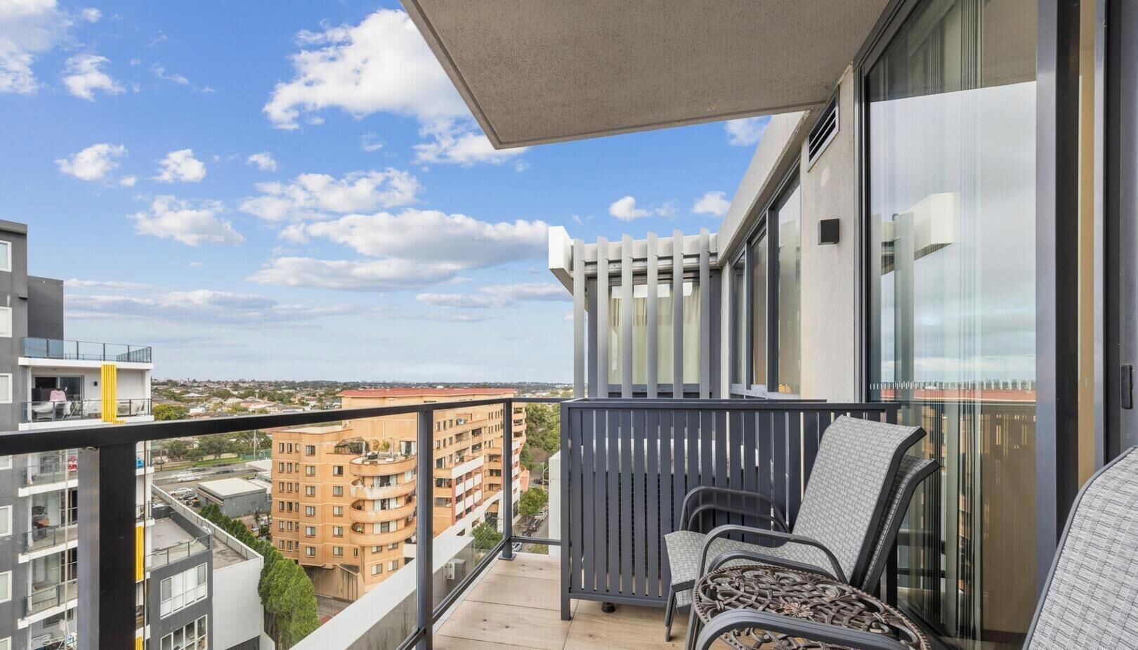 A balcony with a view of surrounding buildings, a pergola, and outdoor seating.