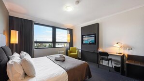 Een hotelkamer met een bed, een bureau, een stoel, een televisie en een raam met uitzicht.