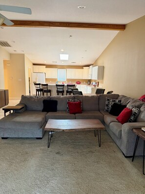 Ein Wohnzimmer mit einer Eckcouch, einem Couchtisch und einer Küche im Hintergrund.