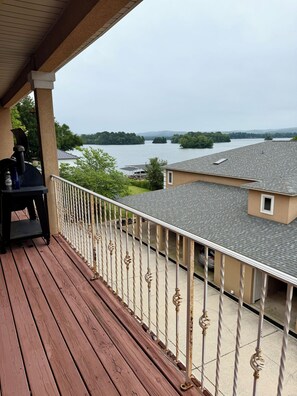 Eine Holzterrasse mit Grill und Gartenmöbeln, mit Blick auf einen See mit Booten und Grünflächen.