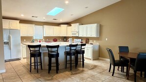 A kitchen with white cabinets, a central island with bar stools, a dining table with chairs, and a ceiling skylight. - Charming 2-bedroom condo on Lake Hamilton (Hot Springs)