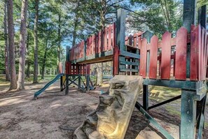 Une aire de jeux avec un toboggan et des structures d’escalade, située dans un parc arboré.