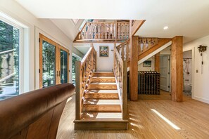 Eine Holztreppe mit Glastrennstäben führt zu einer zweiten Etage, mit einer Holzbank und einem Weinkühlschrank.