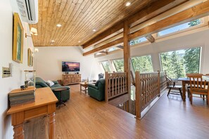 Ein geräumiger Wohnbereich mit Holzboden, einem grünen Sofa, einem Holzessttisch und einem Fernseher.