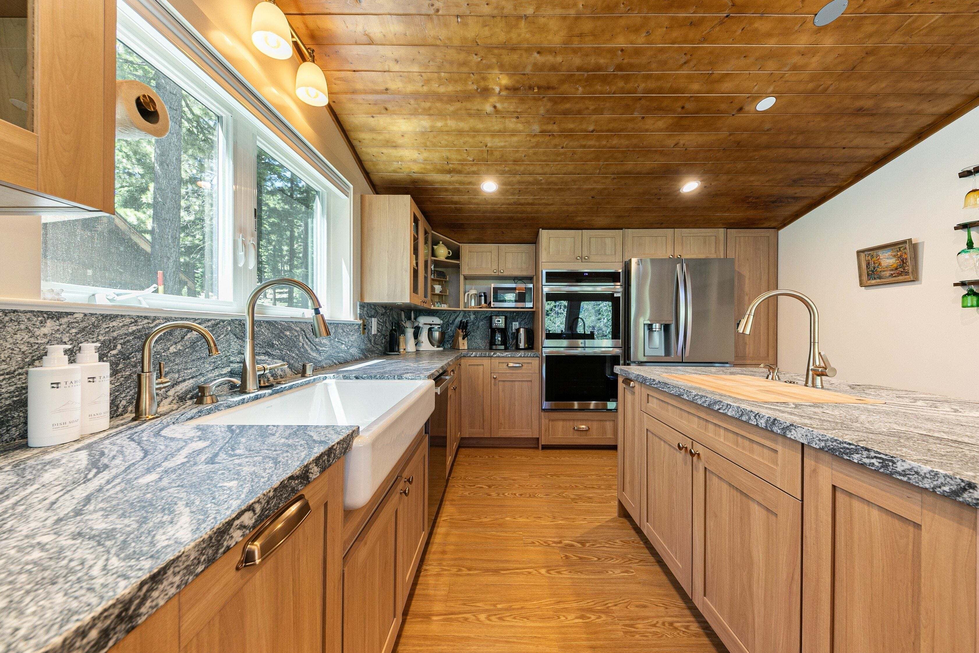 Cocina moderna con armarios de madera, encimeras de granito, electrodomésticos de acero inoxidable y una ventana que ofrece luz natural.