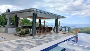 An outdoor pool area with a covered seating area and a view of the landscape.