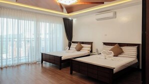 A hotel room with two beds, wooden flooring, a large window with curtains, and a ceiling light fixture.