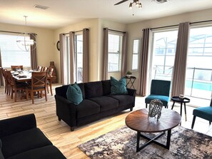 Ein modernes Wohnzimmer mit einer schwarzen Couch, einem runden Couchtisch und einem Essbereich mit einem Holztisch und Stühlen.