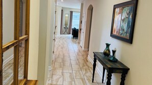 Um corredor com um banco de madeira, uma mesa com vasos e um quadro na parede.