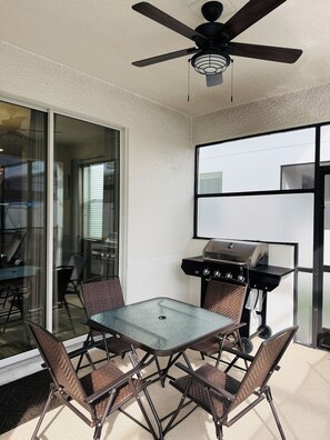 Eine Außenpatio mit einem Glastisch, vier Stühlen, einem Deckenventilator und einem Grill.