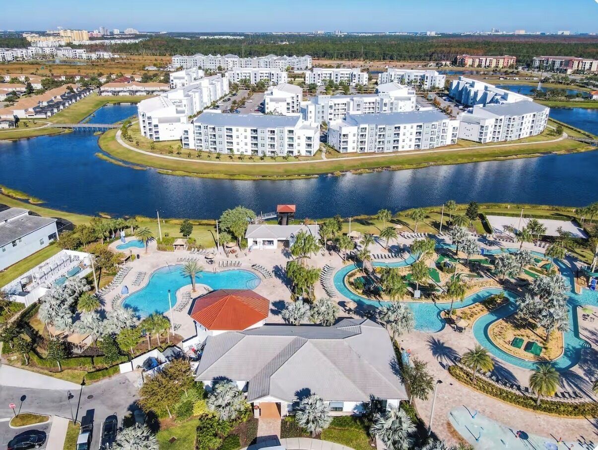 A residential complex with multiple buildings, a central swimming pool, and a lake.