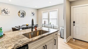 Una cocina moderna con encimera de granito, pileta de acero inoxidable y muebles blancos.