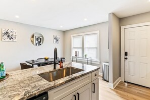 A modern kitchen with a granite countertop, stainless steel sink, and white cabinetry. - Pet-Friendly 2BR in Merion Village (Columbus)