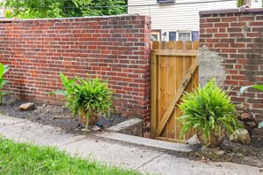 A brick wall with a wooden gate, potted plants, and a concrete pathway. - Pet-Friendly 2BR in Merion Village (Columbus)
