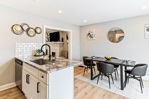 A modern kitchen with a granite countertop, a dishwasher, and a dining area with a table and chairs. - Pet-Friendly 2BR in Merion Village (Columbus)