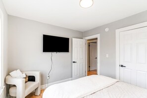 A bedroom with a bed, a chair, a television mounted on the wall, and a door leading to another room. - Pet-Friendly 2BR in Merion Village (Columbus)