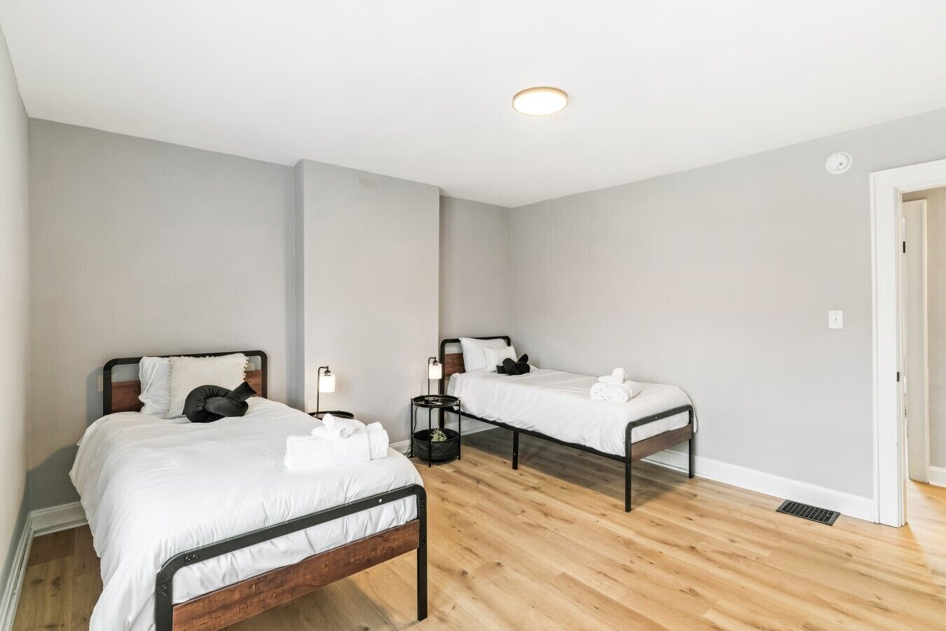 A hotel room with two single beds, a bedside table with a lamp, a wooden floor, and a door.