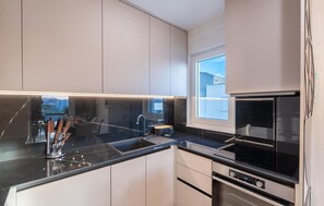 Een moderne keuken met een zwart aanrecht, roestvrijstalen apparatuur en een raam met uitzicht op een woonwijk.