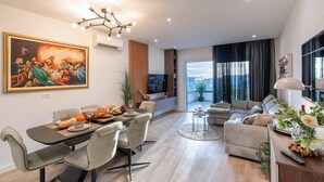 Un salon moderne comprenant un coin repas, un ensemble de canapés, un téléviseur et un grand tableau accroché au mur.