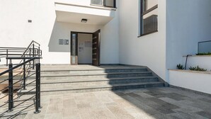 Une entrée moderne avec un escalier menant à une porte, un petit espace extérieur avec des marches et une rambarde en métal.