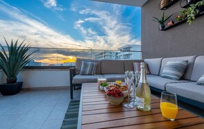 Eine Dachterrasse mit einer Couch, einem Esstisch mit Speisen und Getränken und Blick auf den Sonnenuntergang.