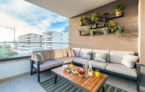 A balcony with a sofa, a dining table, and potted plants. - Nice apartment in Makarska with lake view (Makarska)