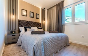 Een slaapkamer met een groot bed, nachtkastje, een wandlamp en een raam met gordijnen.