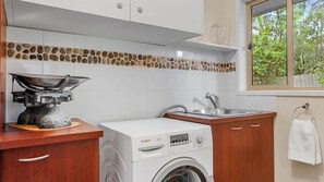 A compact kitchen with a washing machine, a stove, and a window with a view of greenery. - Saltwater Sanctuary | Fireplace & Walk to Beach (Mount Martha)