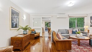 Ein geräumiges Wohnzimmer mit einem Holztisch, Ledersofas und einem Essbereich mit Blick ins Grüne.