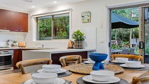 Uma cozinha moderna com área de jantar, grandes janelas e vista para o verde.