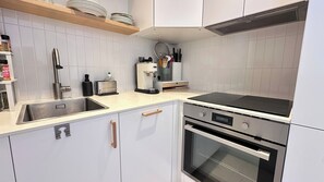 A modern kitchen with white cabinetry, a stainless steel sink, a built-in oven, and a black induction cooktop. - Charming apartment with lift near Marx Dormoy (Paris)