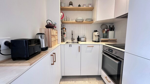 Eine kleine Küche mit weißen Schränken, einem eingebauten Backofen und einer Kaffeemaschine.