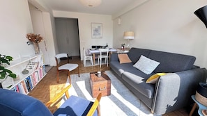 A modern living room with a grey sofa, wooden coffee table, and a dining area with a white table and chairs. - Charming apartment with lift near Marx Dormoy (Paris)