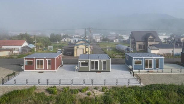 Una hilera de edificios pequeños de una sola planta y tejado plano, probablemente utilizados como alojamientos temporales u oficinas, ubicados en una zona rural con vistas despejadas del paisaje circundante.