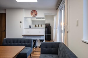 A modern kitchen with a clock, a refrigerator, and a dining area with a table and chairs. - Ocean Stay (Shiraoi)