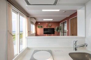 A modern kitchen with a large window, a built-in oven, and a flat-screen TV mounted on the wall. - Ocean Stay (Shiraoi)