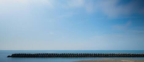 A coastal scene with a breakwater extending into the sea, a sandy beach, and a clear sky.