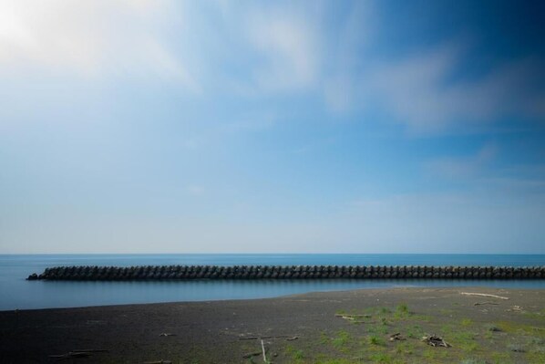 A coastal scene with a breakwater extending into the sea, a sandy beach, and a clear sky.