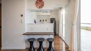 Una cocina moderna con encimera de madera, tres taburetes negros, un reloj y vistas amplias a través de grandes ventanales.