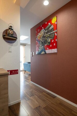 A hallway with a red wall, a clock, and a painting of a person holding a gun.