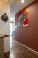 A hallway with a red wall, a clock, and a painting of a person holding a gun.