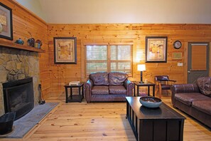 Ein rustikales Blockhaus-Interieur mit Kamin aus Naturstein, Ledersofas, Holzböden und Holzwänden.