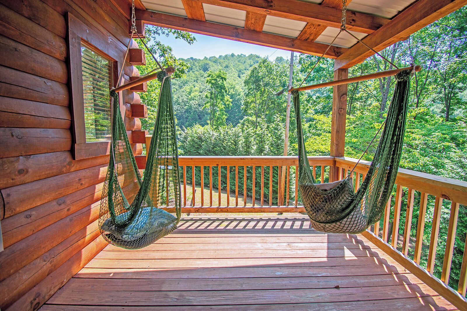 A wooden deck with two green hammocks and a wooden railing overlooking a forest.