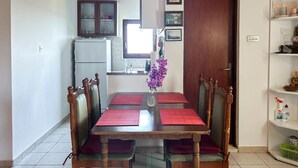 Een eetgedeelte met een houten tafel en stoelen, een vaas met paarse bloemen, en een keuken op de achtergrond.