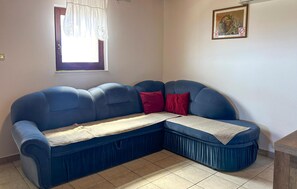 Ein blaues Ecksofa mit einer beige farbenen Decke, einem roten Kissen und einem gerahmten Bild mit Früchten an der Wand.