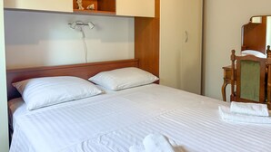 Een net opgemaakt bed met witte lakens en kussens, een houten hoofdbord en een nachtkastje met spiegel.