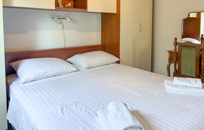 Ein ordentlich bezogenes Bett mit weißen Leinen und Kissen, ein Holzkopfstück und ein Nachttisch aus Holz mit einem Spiegel.