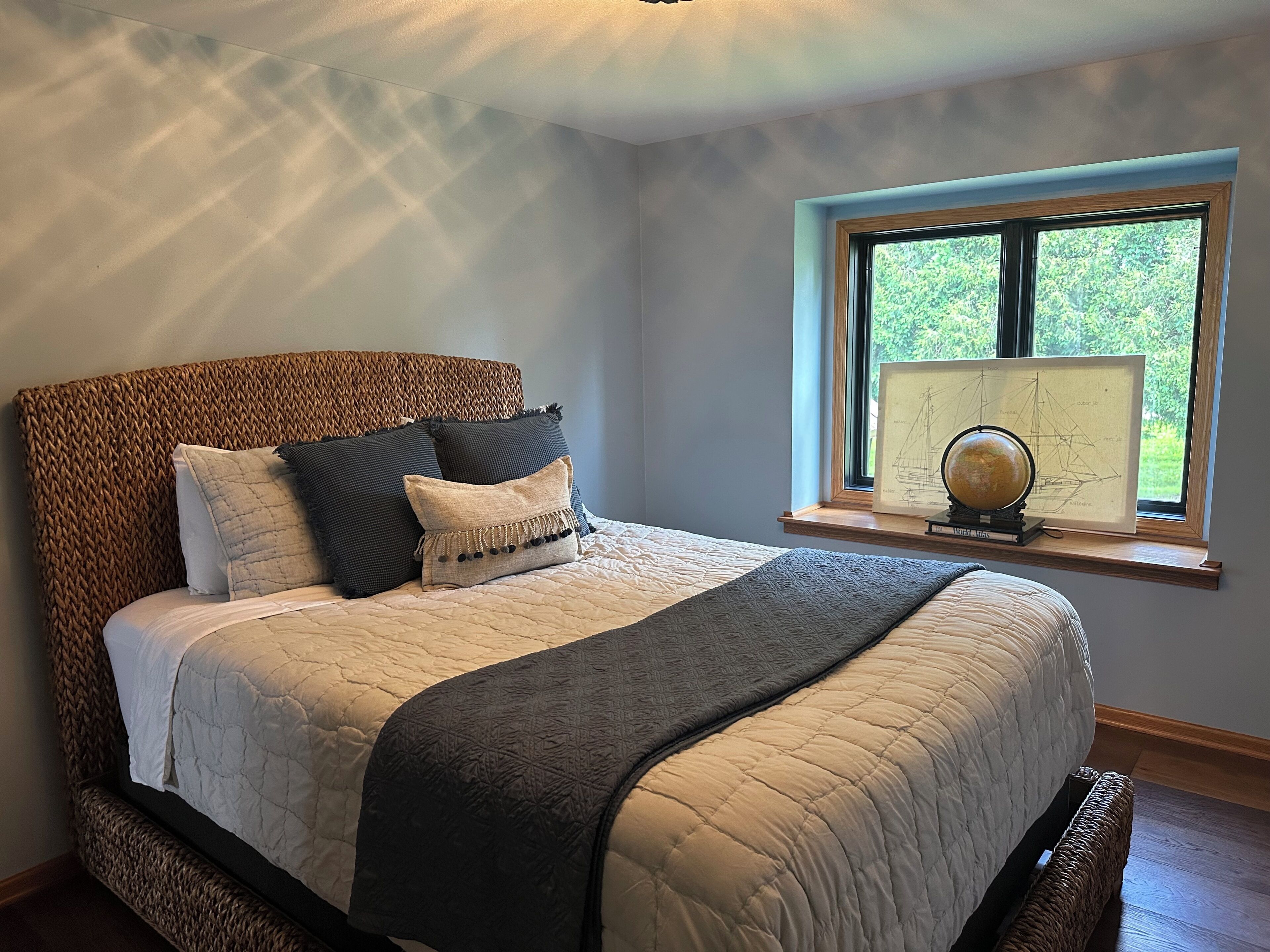 A bed with a woven headboard, a window with a view of greenery, and a globe on the windowsill.